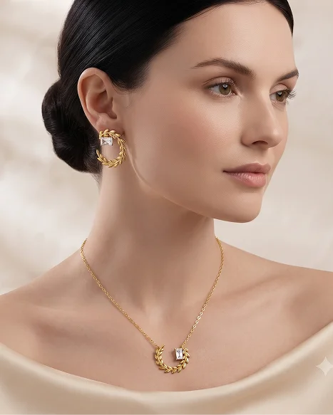 A woman with dark hair in a bun models a gold crescent moon pendant necklace and matching twisted hoop earrings with clear gemstones, set against a soft beige background.