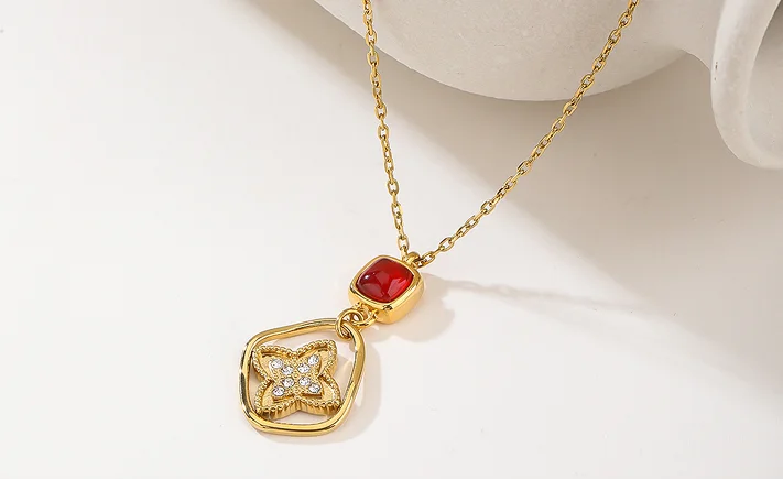 Gold pendant necklace with a square gold frame, a small red gemstone, and a butterfly design set with clear crystals, displayed on a white background.
